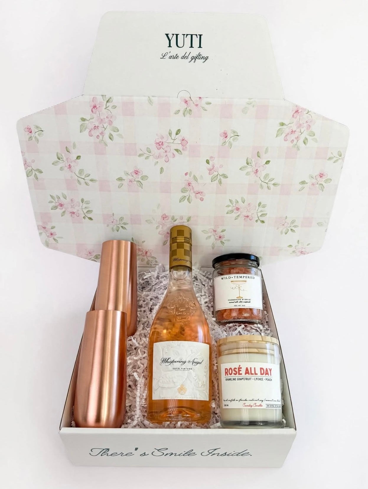 A curated gift box set by Yuti containing a bottle of Rosé Champagne, a rose gold cocktail shaker, a jar of rose petals, and a candle, all arranged inside a white box with a pink floral patterned lid.