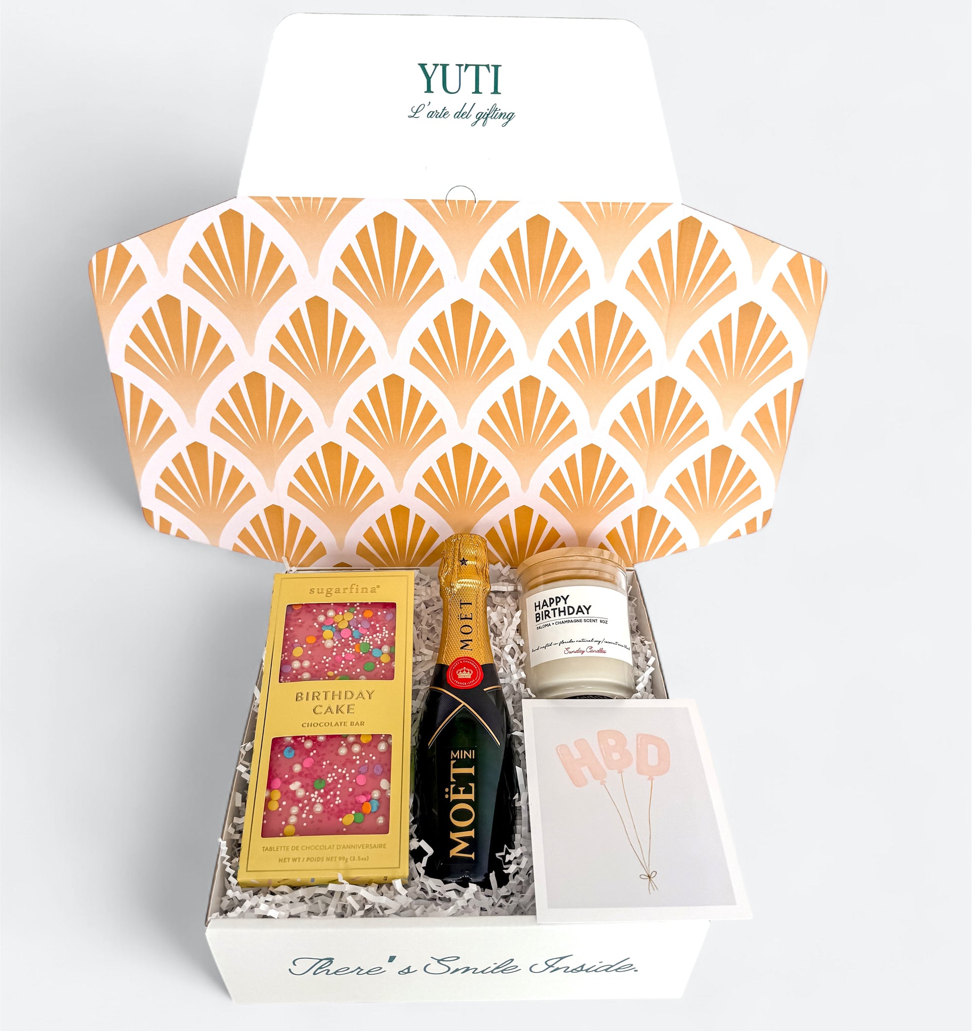 Gift box with shell pattern, containing a bottle of Moët & Chandon, a box of chocolates, and a candle, branded 'YUTI'.